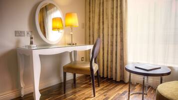 A hotel room with a white console table, a chair, a round table, a mirror, and a lamp.
