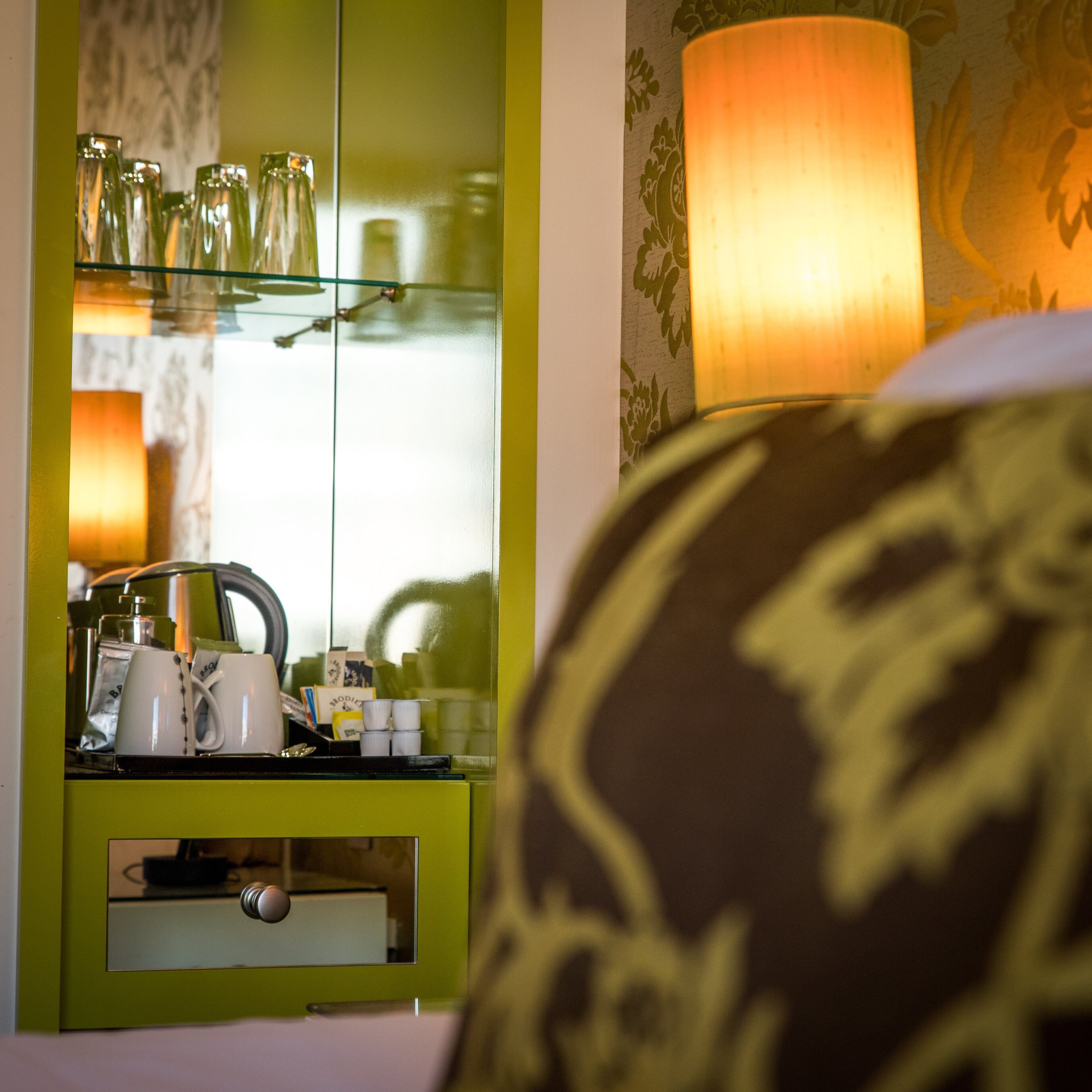 A room with a green minibar, a lamp, and a bed with a patterned pillow.