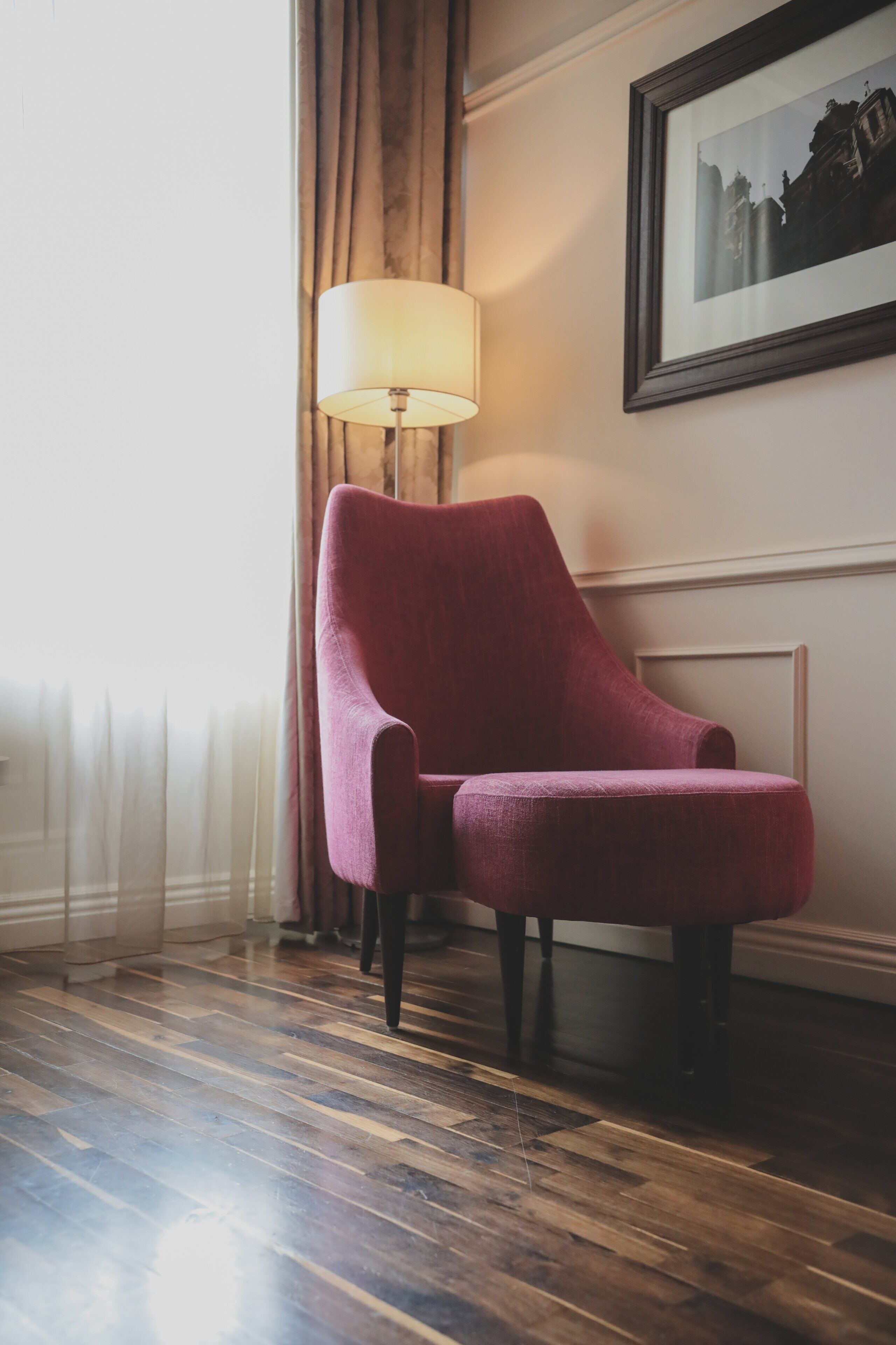 A room with a wooden floor, a red armchair, a lamp, and a framed picture on the wall.