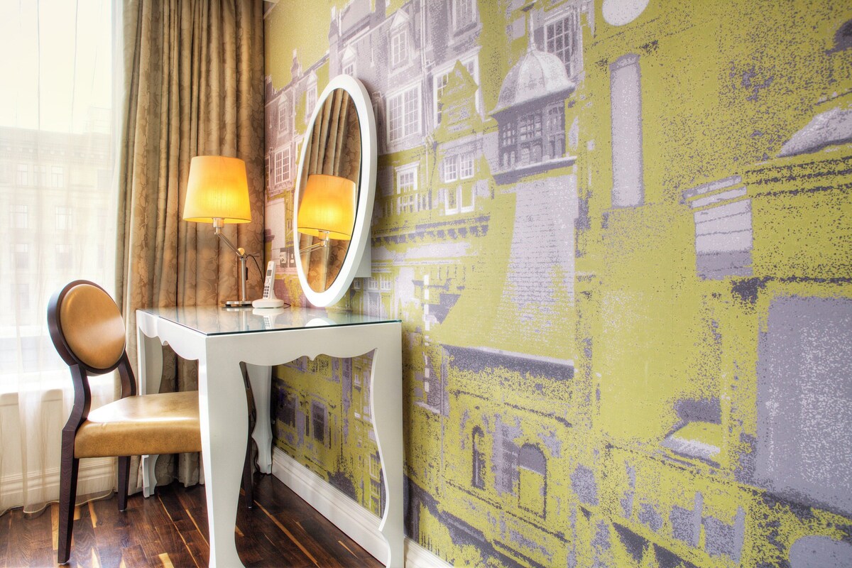 A room with a glass table, a chair, a mirror, and a wall with a yellow and grey patterned wallpaper.