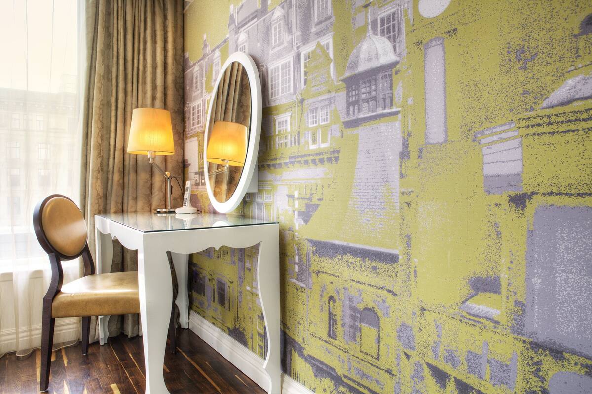 A room with a glass table, a chair, a mirror, and a wall with a yellow and grey patterned wallpaper.