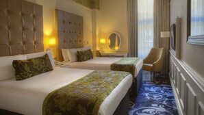 Habitación de hotel con dos camas, un cabecero grande y acolchado, un espejo, una silla y suelo alfombrado.