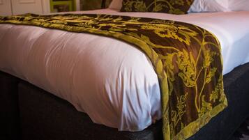 A neatly made bed with a white and gold patterned bedspread, a wooden headboard, and a wall-mounted lamp.