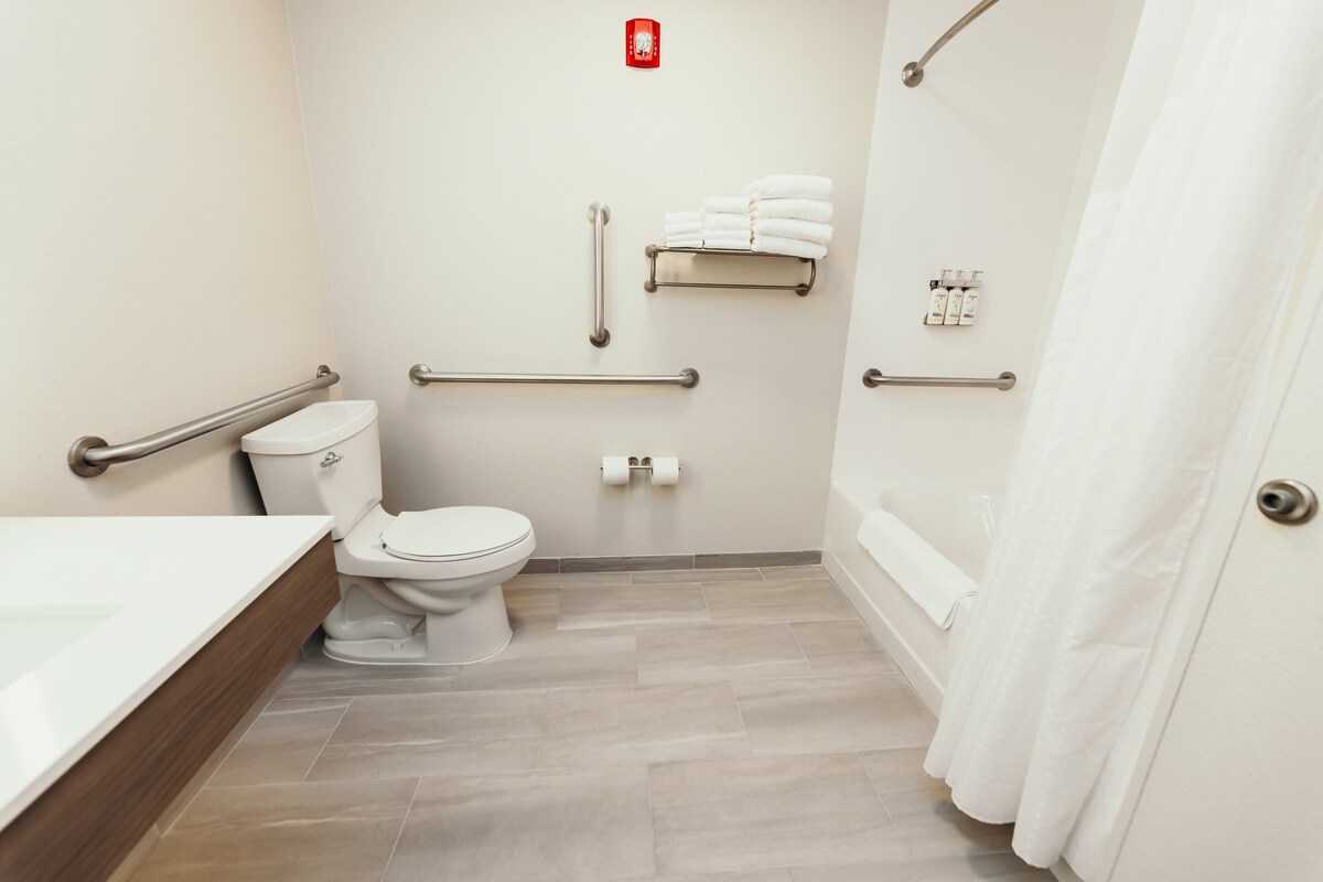 A bathroom with a toilet, bidet, handrails, a towel rack, and a shower curtain.