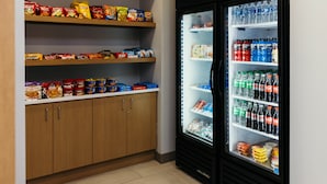 Eine Küchenzeile mit Regalen voller Snacks und einem Kühlschrank mit Wasser und Limonade.