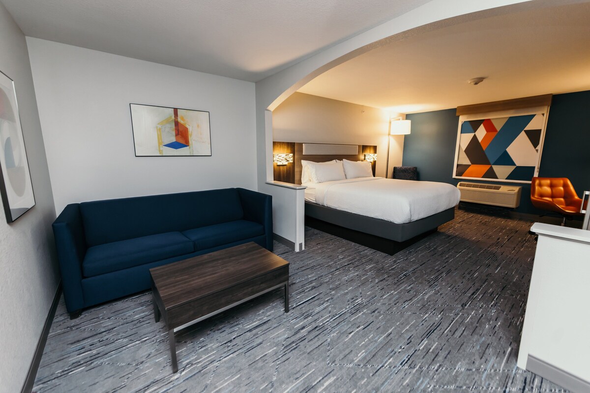 A hotel room with a bed, a sofa, a small table, and a painting on the wall.