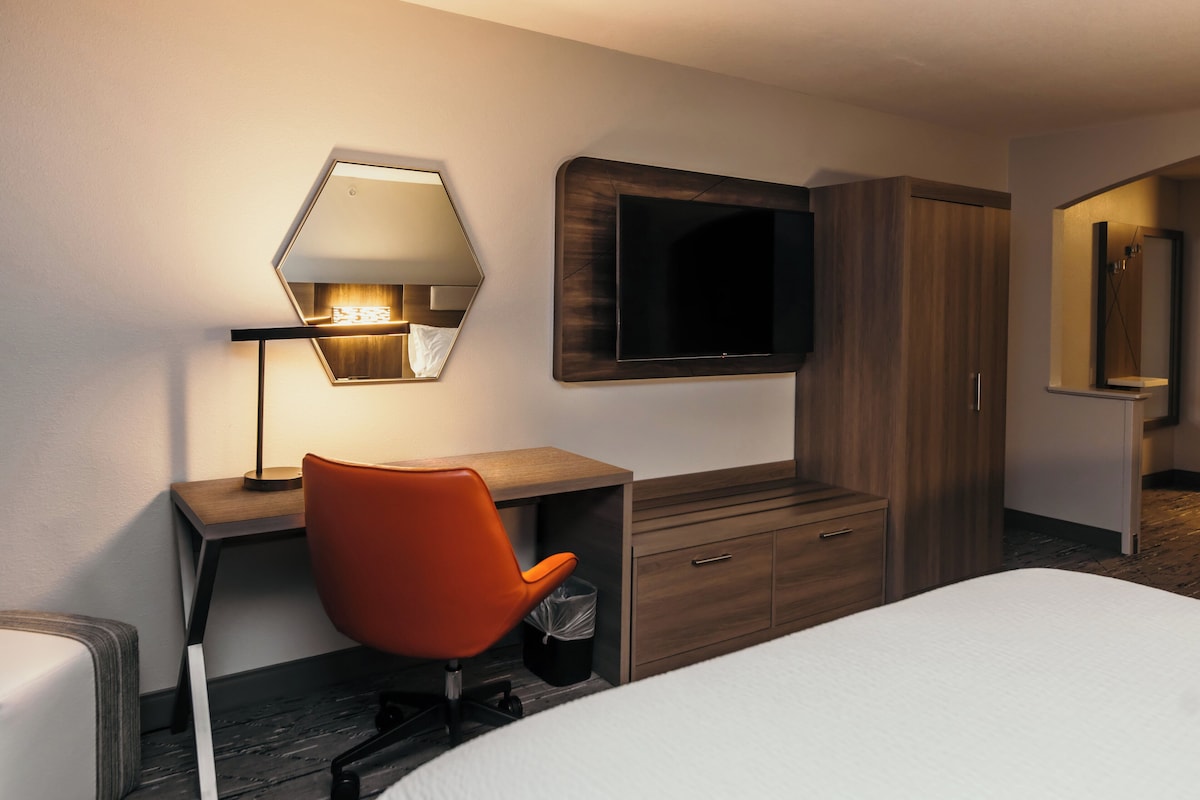 Una camera d'albergo con un letto, una scrivania con sedia, una televisione a parete e un armadio in legno.