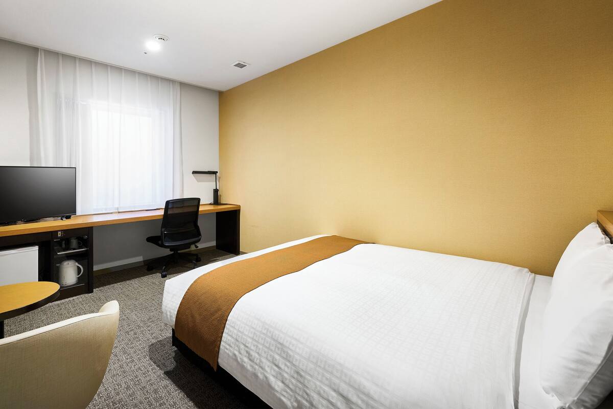 A hotel room with a bed, a desk with a computer, a chair, and a television.