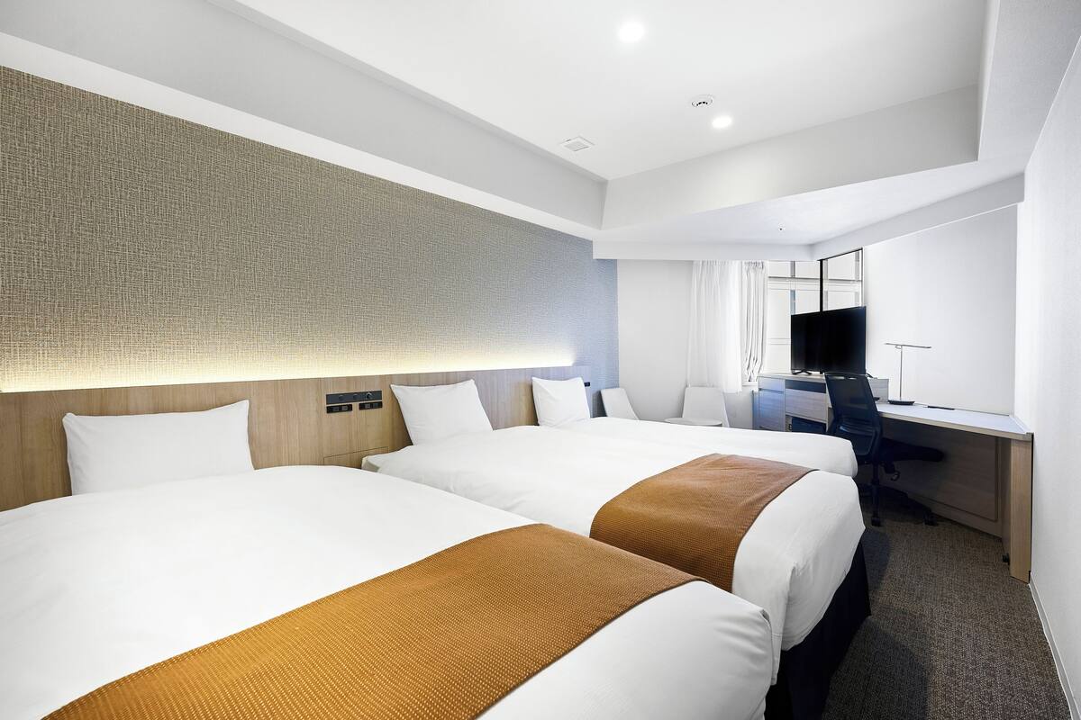 A hotel room with two beds, a desk, and a television.