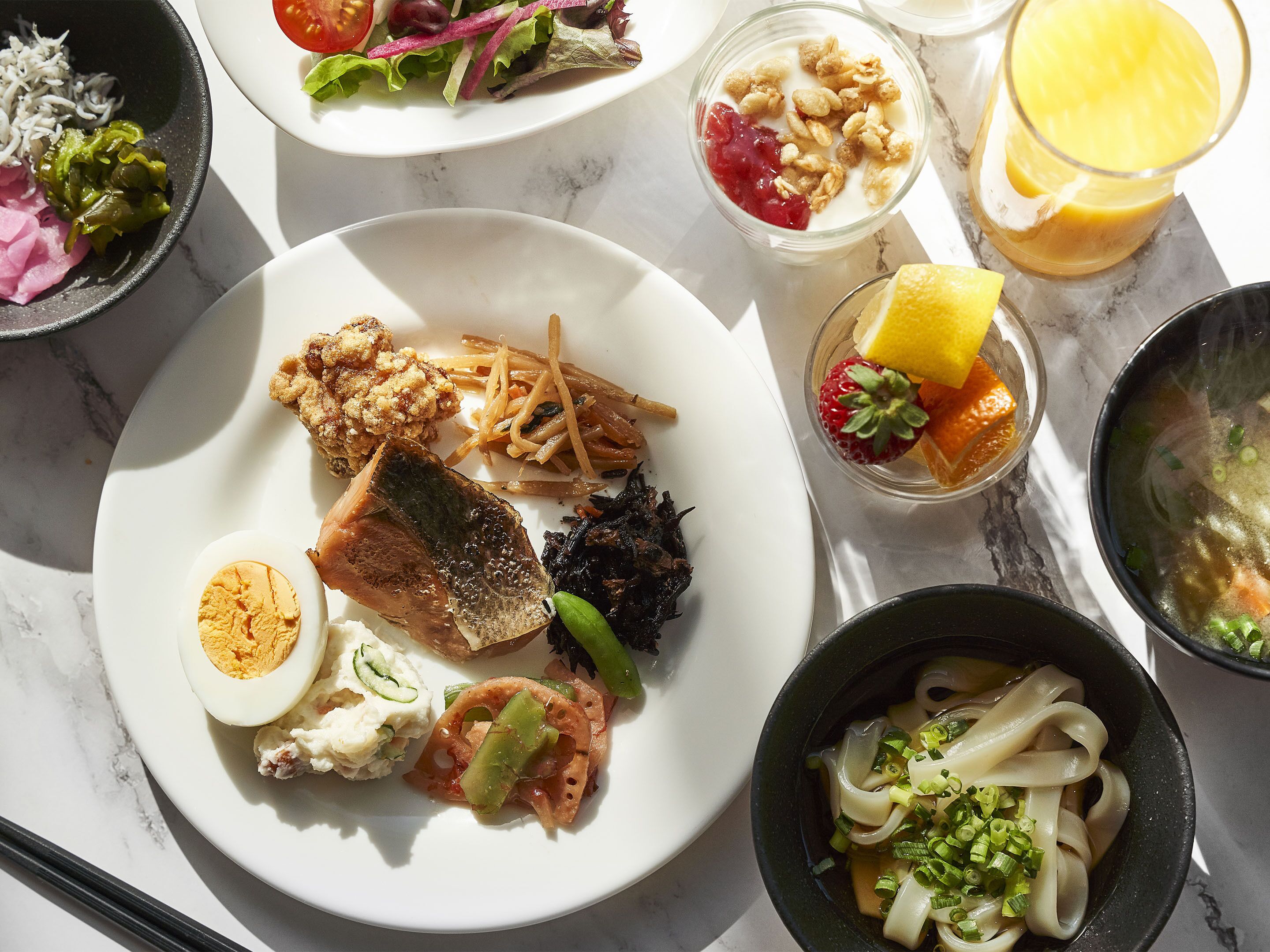 A variety of dishes including a plate with a boiled egg, fish, and vegetables, a bowl of soup, and a glass of orange juice.