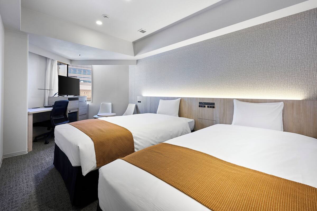 A hotel room with two beds, a desk, a chair, a TV, and a large window.
