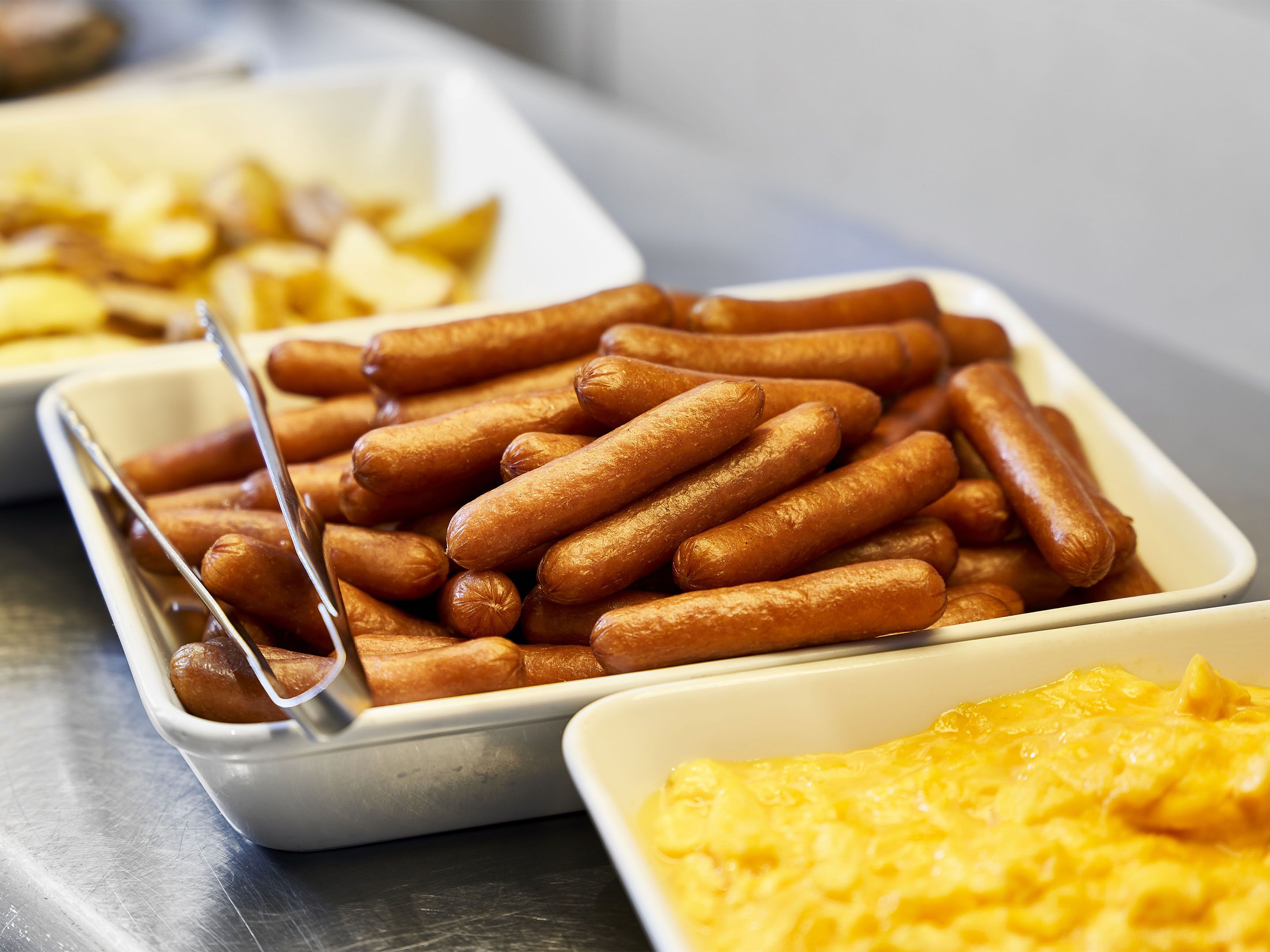 A buffet with hot dogs, potato wedges, and macaroni and cheese.