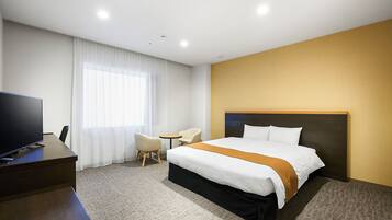 A hotel room with a large bed, a desk with a television, a small table, and a chair.