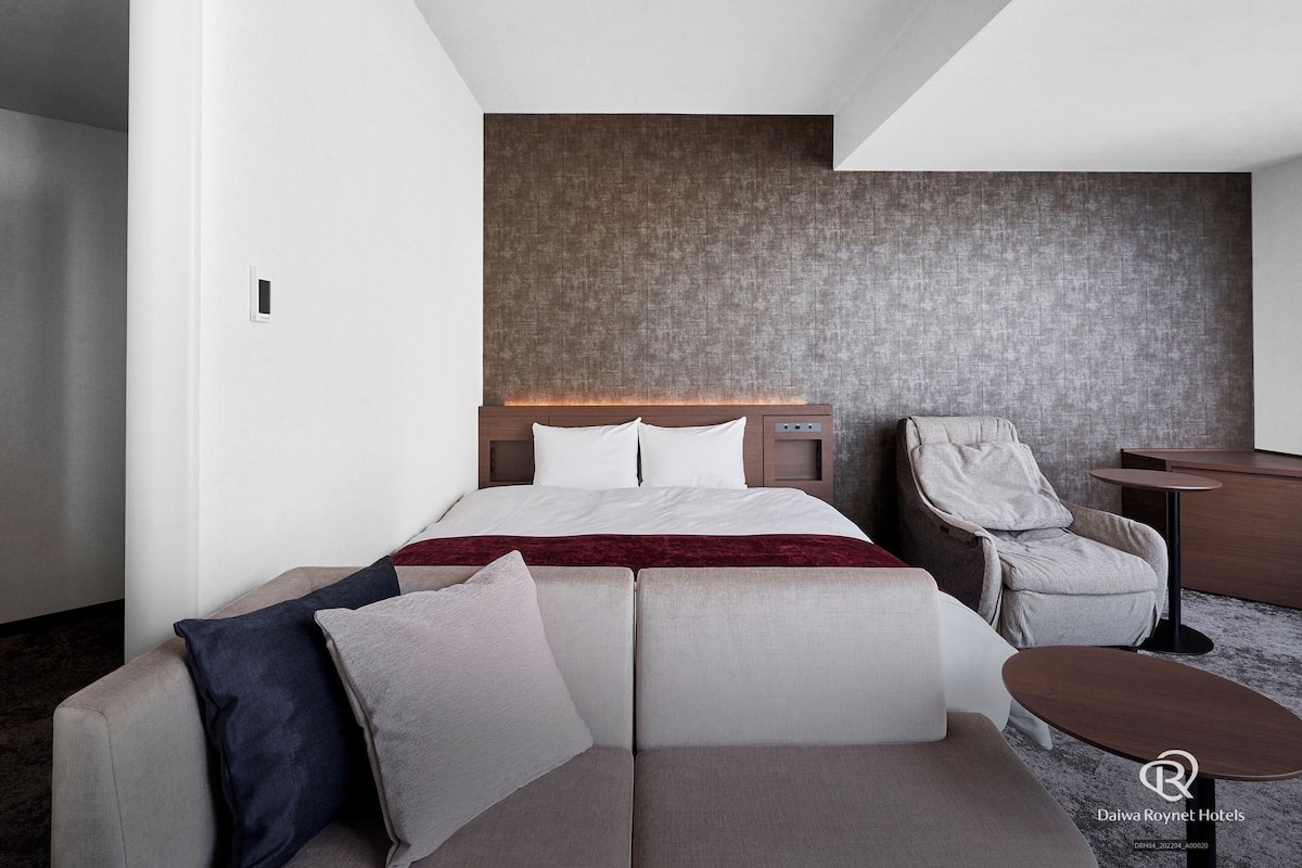 A modern hotel room with a bed, a sofa, a chair, and a small table.
