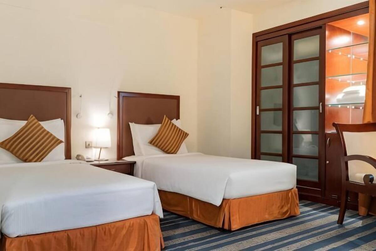 A hotel room with two beds, a desk, a chair, a wardrobe, and a lamp.
