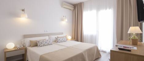 Habitación de hotel con una cama grande, mesitas de noche, un escritorio con lámpara, televisor y una planta en maceta.