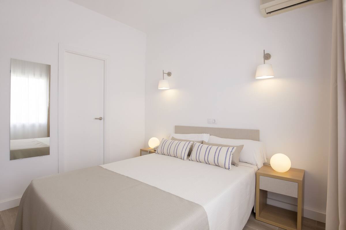 Quarto minimalista com cama, abajures, mesa de cabeceira e espelho.