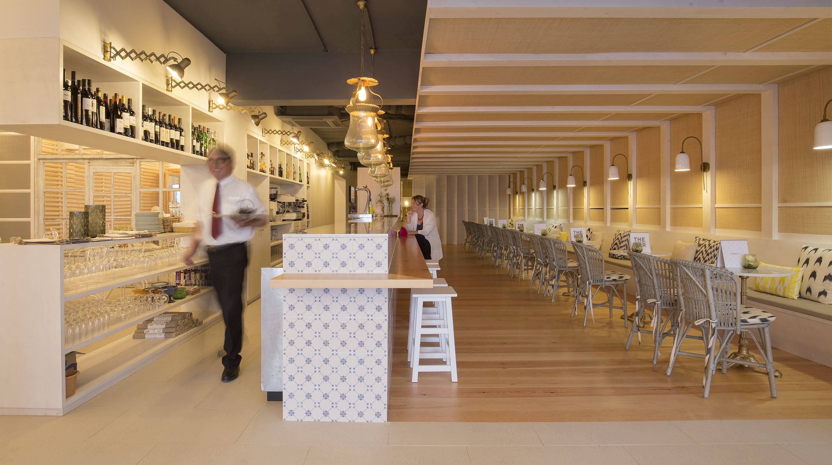 Un área de bar moderna con una barra larga, estantes llenos de botellas y sillas de mimbre.