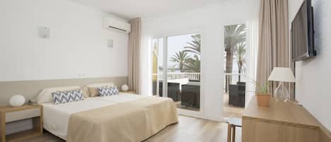 A hotel room with a bed, bedside table, lamp, TV, and a view of the outdoors.