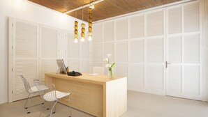 A reception desk with a computer, a vase with flowers, and a chair in a room with white lockers and a wooden ceiling. -  Hotel Cabot Romantic - Adults Only (Pollenca)