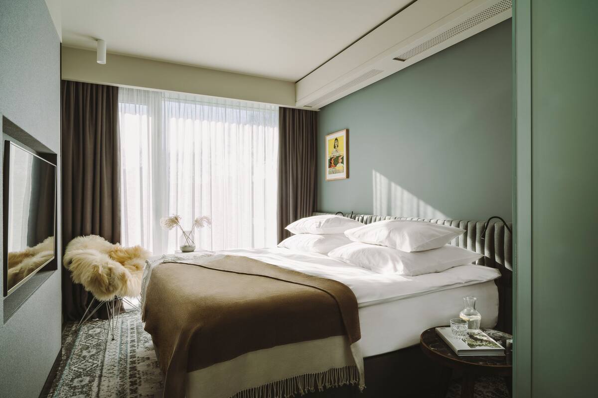 Une chambre d’hôtel avec un lit, une télévision, une petite table avec un livre et un fauteuil décoratif.