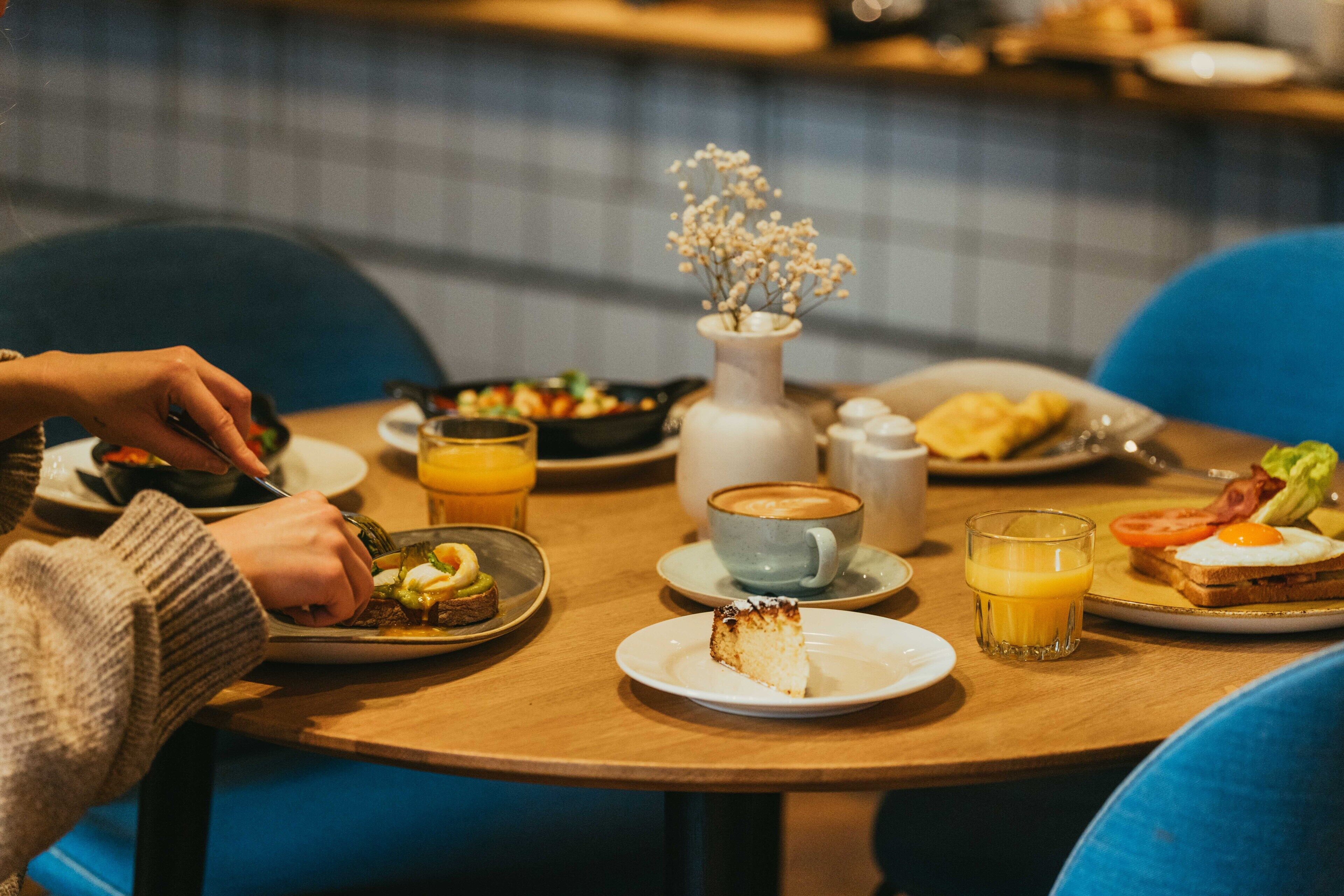 Un desayuno con varios alimentos en platos, una taza de café y un vaso de zumo de naranja sobre una mesa de madera.