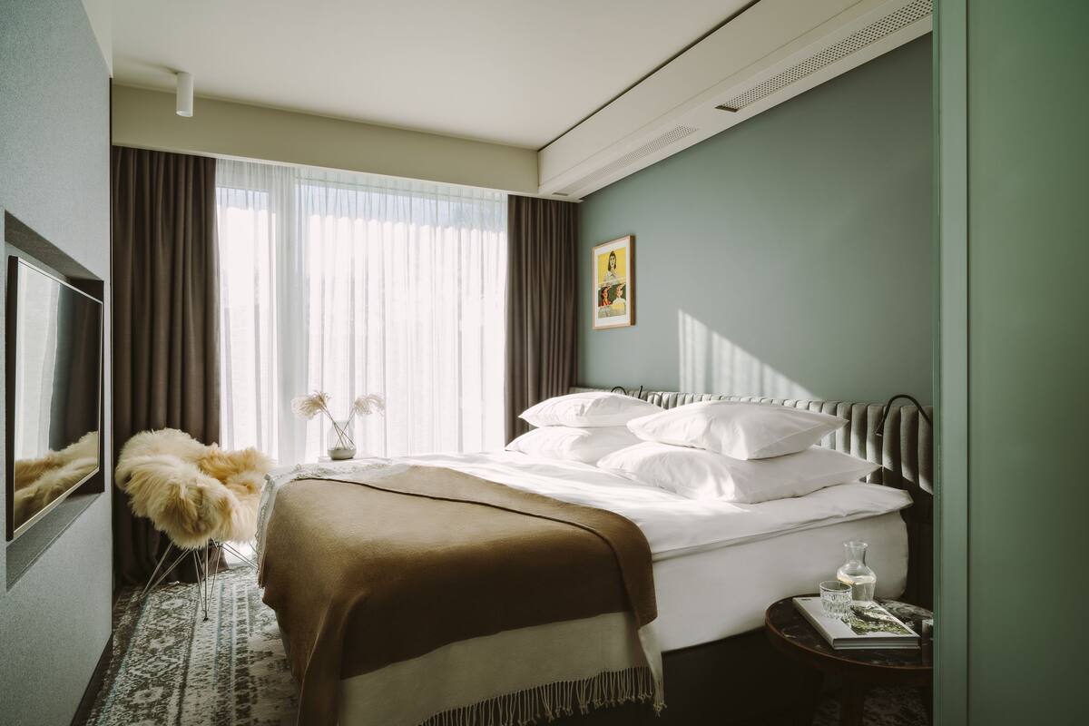 Une chambre d’hôtel avec un lit, une télévision, une petite table avec un livre et un fauteuil décoratif.