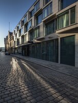Un bâtiment moderne à plusieurs étages, doté de grandes fenêtres et situé devant une rue pavée.