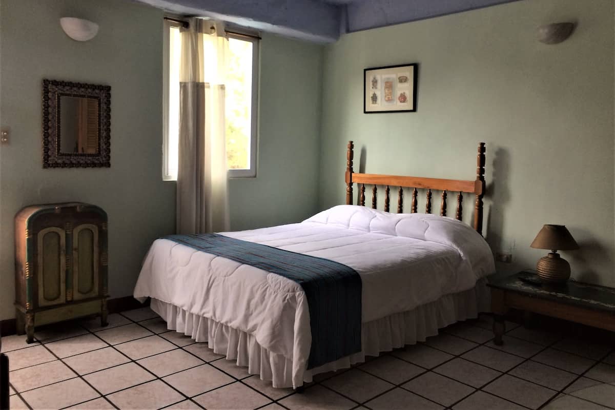 A room with a bed, a nightstand, a lamp, a dresser, a framed picture, and a window with curtains.