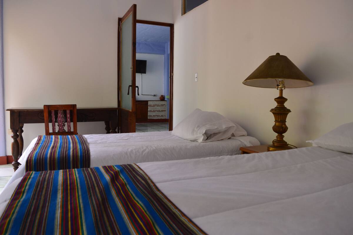 A hotel room with two beds, a wooden nightstand, a lamp, and a mirror.
