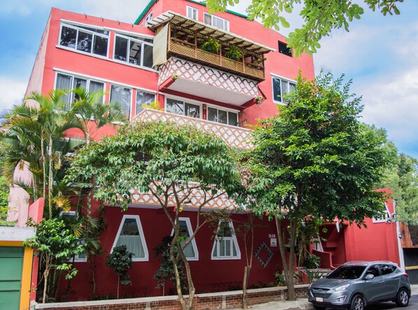 Un immeuble rouge à deux étages, doté de nombreuses fenêtres, d’un balcon et d’une voiture garée devant.