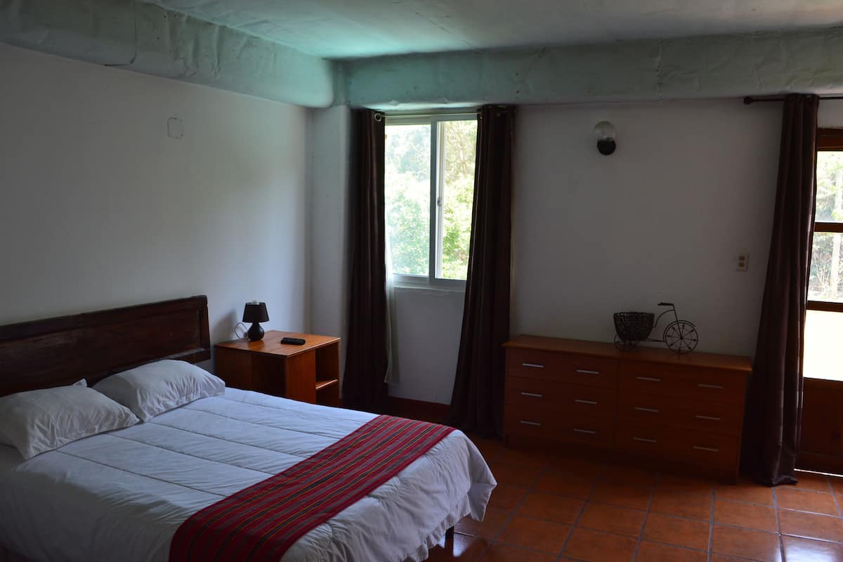 A bedroom with a bed, a dresser, a nightstand, a window with curtains, and a bicycle on the dresser.