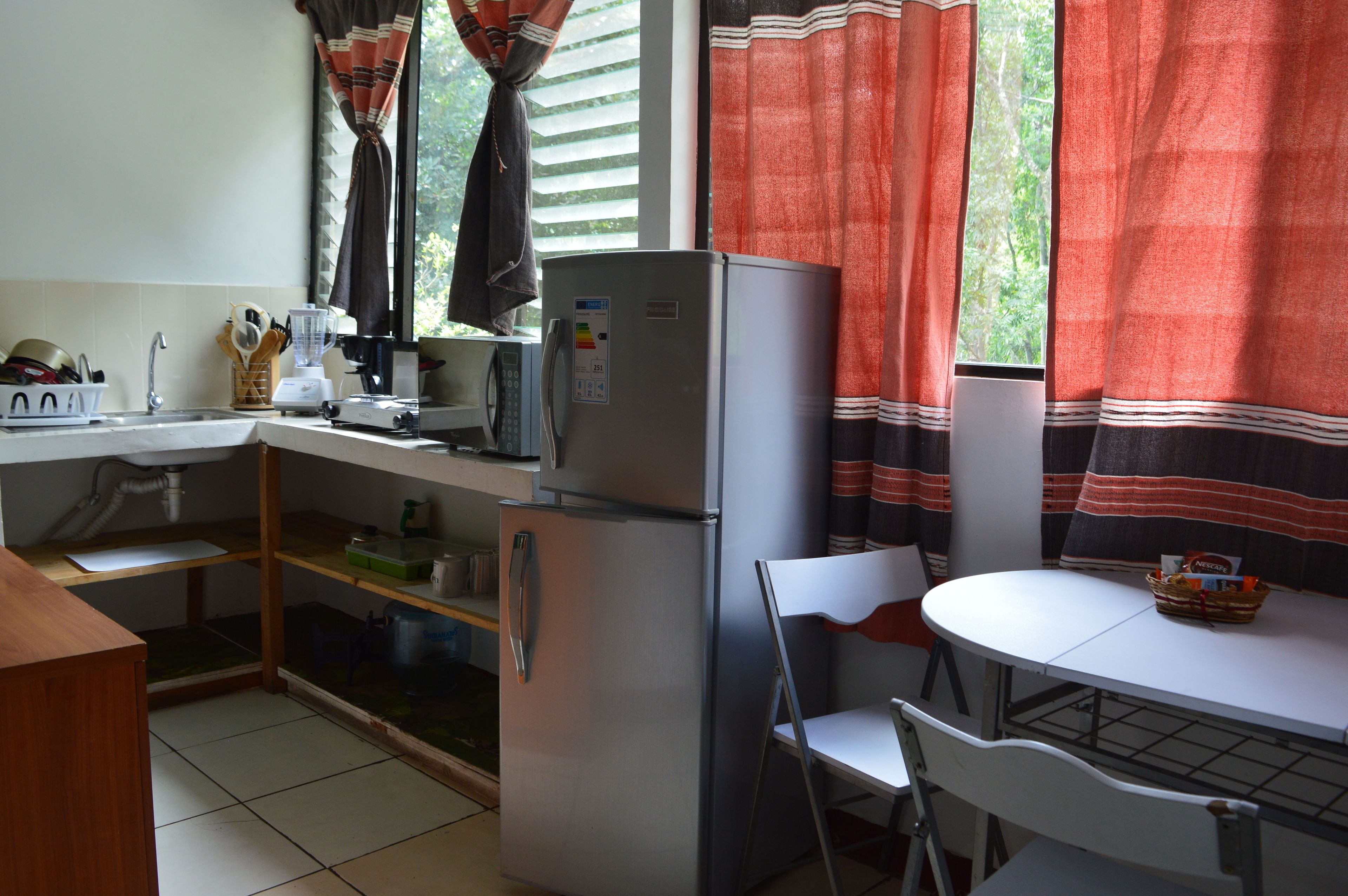 Una cocina compacta con refrigerador, pileta y un pequeño comedor con mesa y sillas.