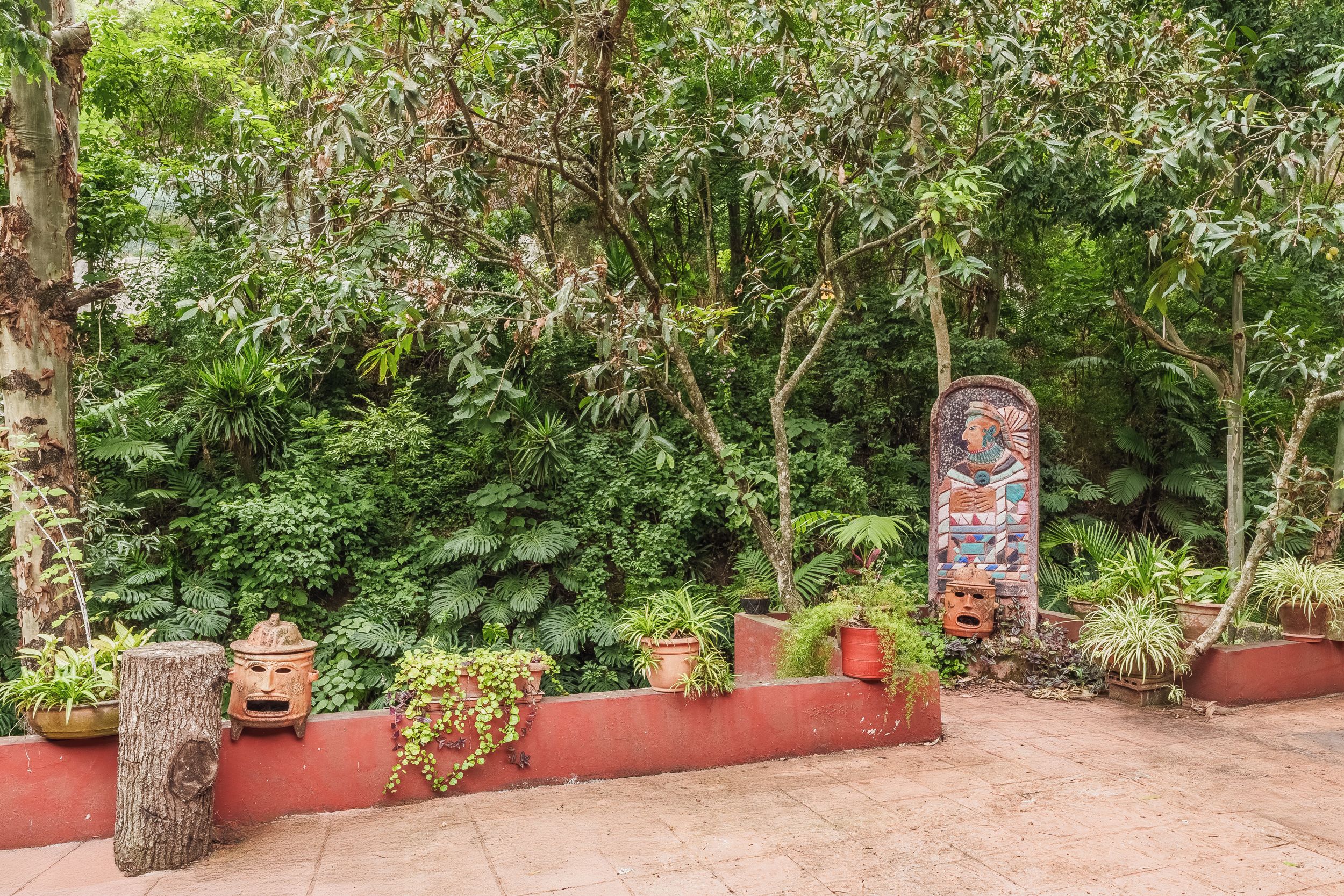 Un jardín con diversas plantas y un muro decorativo con un mosaico.