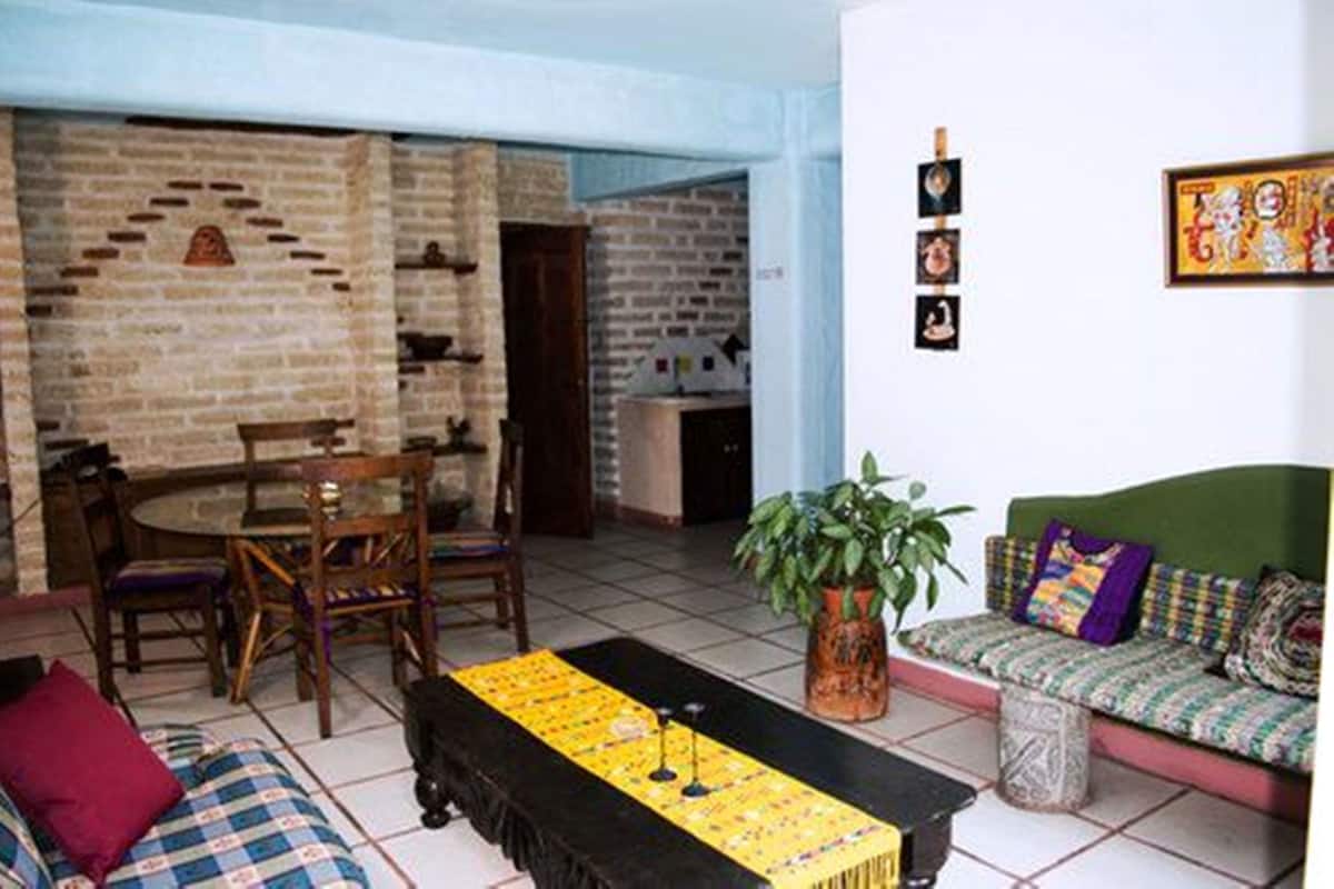A living room with a brick wall, a green sofa, a dining table with chairs, and a coffee table with a plant.