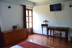 Un dormitorio con cama, cómoda, televisor y una pequeña mesa con silla.