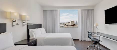 A hotel room with two beds, a desk, a chair, a TV, and a window with a city view.