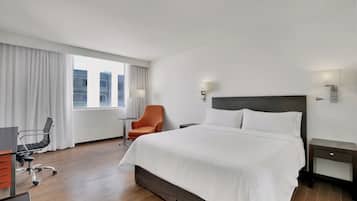 Habitación de hotel con una cama grande, un escritorio con silla, una mesita pequeña y una ventana con cortinas.