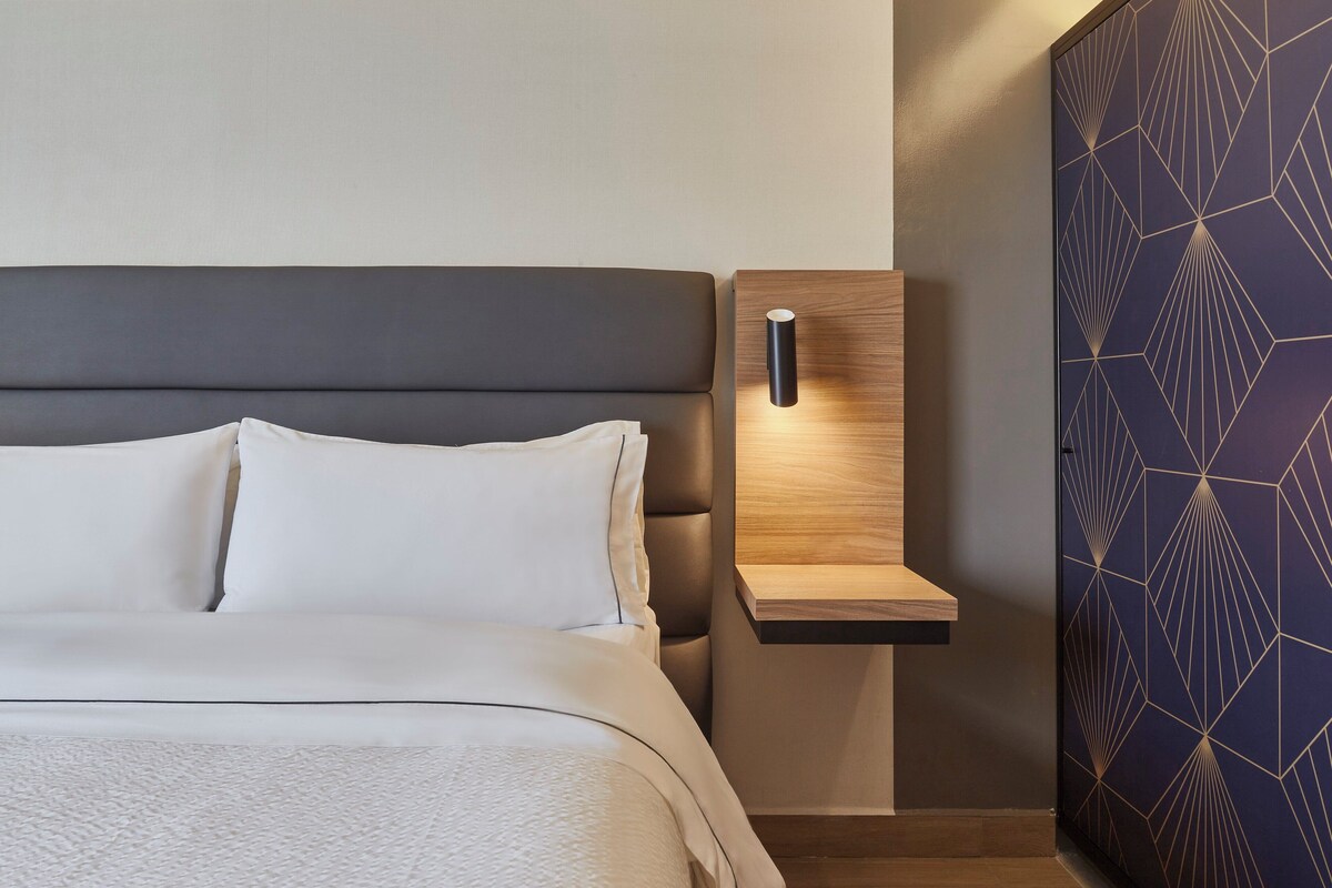 A modern bedroom with a bed, a nightstand, and a wall with geometric patterns.