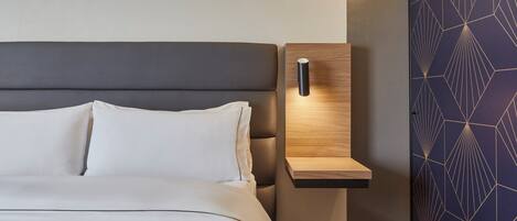 A modern bedroom with a bed, a nightstand, and a wall with geometric patterns.