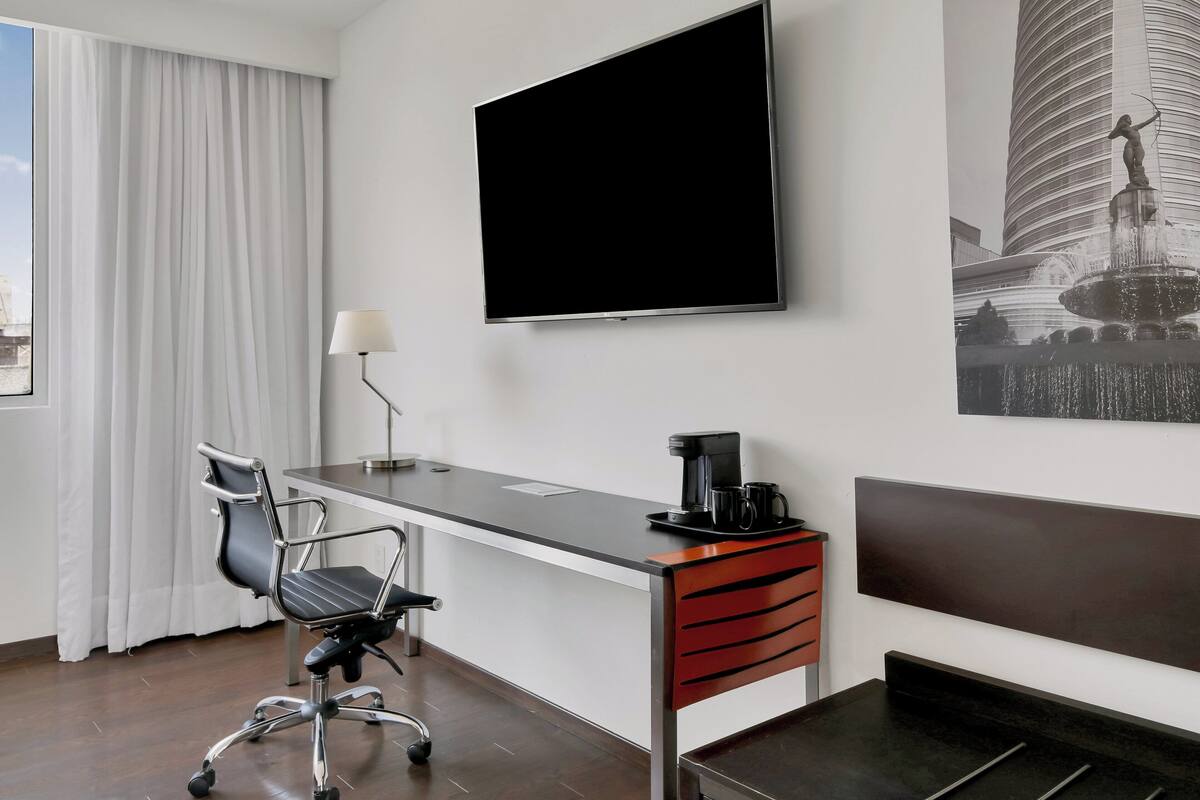 A hotel room with a desk, chair, flat-screen TV, coffee maker, and a bed.