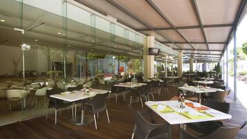 An indoor dining area with glass walls, wooden flooring, and tables set for dining.