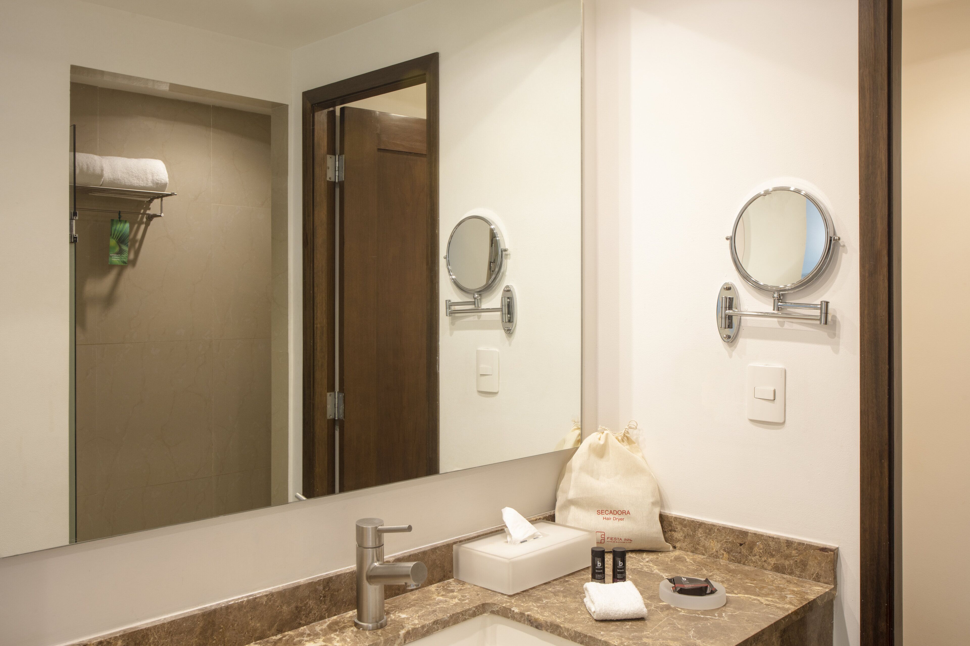 A hotel bathroom with a sink, mirror, towel rack, and a door leading to a shower area.
