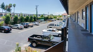 A parking lot with several cars and a truck, a building with a covered walkway, and a row of windows. - Motel Moonlight (Anaheim)