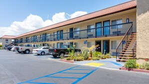 A motel with multiple rooms, a parking lot, and a staircase leading to the entrance. - Motel Moonlight (Anaheim)