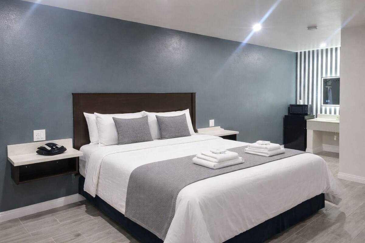 A modern hotel room with a large bed, bedside tables, a built-in TV, and a bathroom with a mirror and sink.