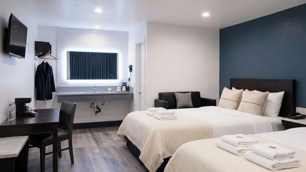 A hotel room with two beds, a desk, a chair, a TV, and a window with curtains. - Motel Moonlight (Anaheim)