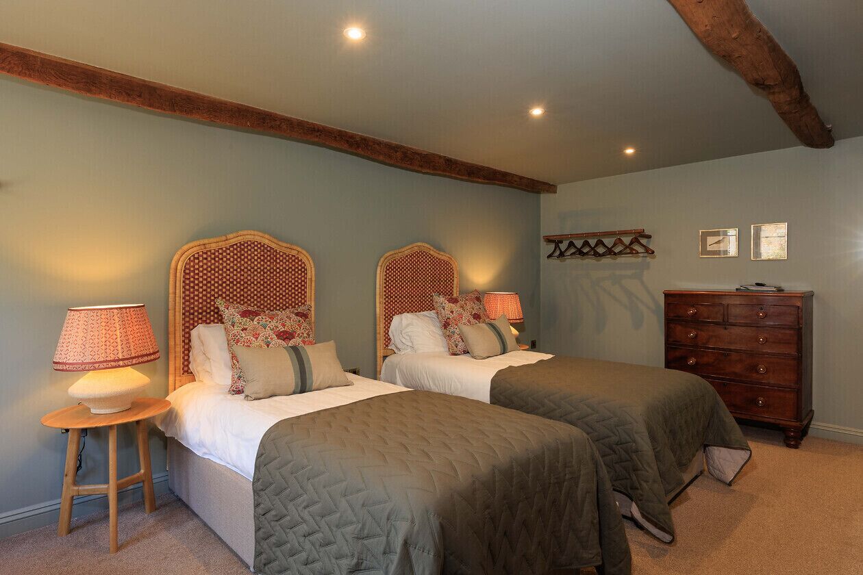 Une chambre avec deux lits, une commode en bois et une petite table avec une lampe.
