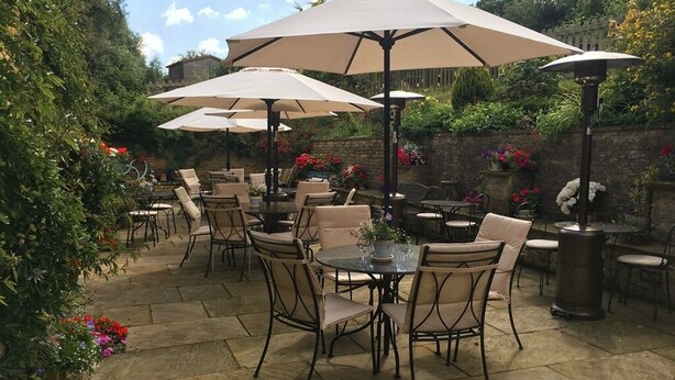 An outdoor patio with multiple tables and chairs, surrounded by large umbrellas and potted plants.