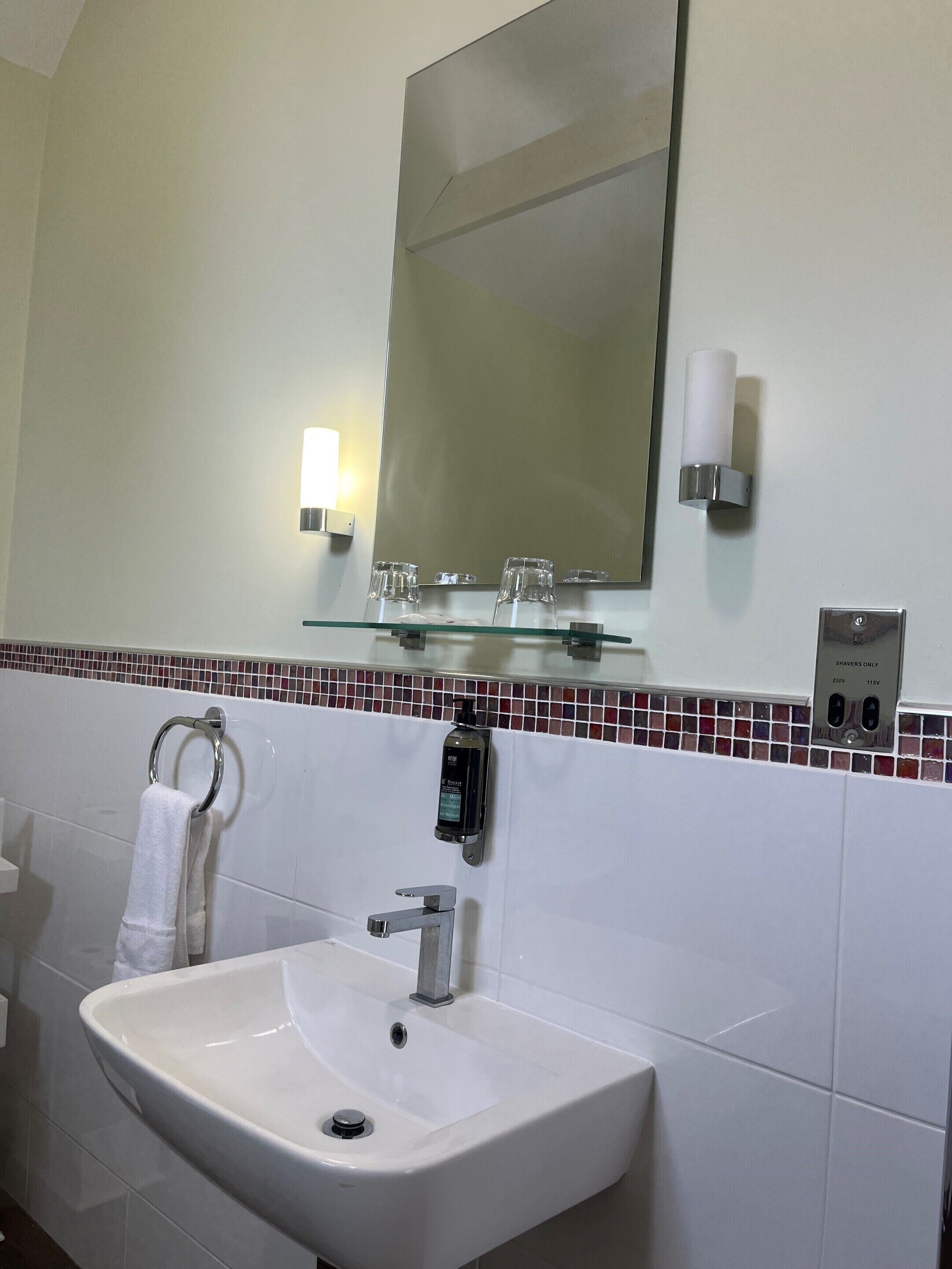 A bathroom with a white sink, a mirror, a towel rack, and a soap dispenser.